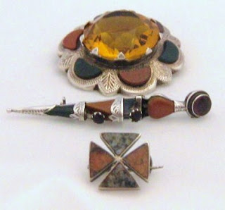 A collection of old Scottish agate jewellery. From top: a vintage 1970s brooch with huge yellow centre stone, a 1920s silver dirk pin in the shape of a tiny dagger, and a tiny early Victorian cross brooch.