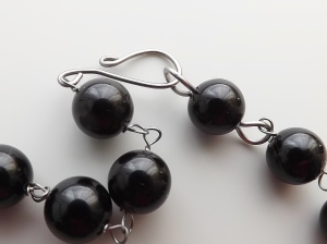 image shows a close up of some round black agate beads on titanium wire links