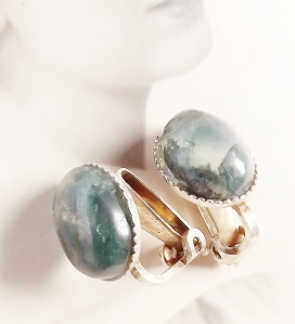 image of a pair of clip on silver earrings, each set with a large oval moss agate gemstone. These moss agates are colourless as a base, with lots of dark green inclusions which give the appearance of internal plants and ferns