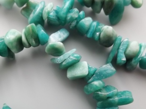 image shows a close up photo of a string of dark greenish-blue amazinite nugget beads, with faint white stripey striations on them