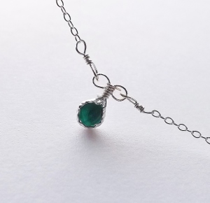 image shows a very small round cut rare dioptase gemstone set into a sterling silver bezel pendant, with two curved loops at the top for the bail. which is attached to a necklace chain.