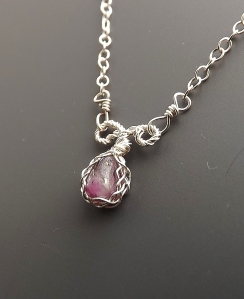 image shows a ruby in matrix stone from Norway, set into a sterling silver pendant that has a Celtic style patetrn wire design around the sstone