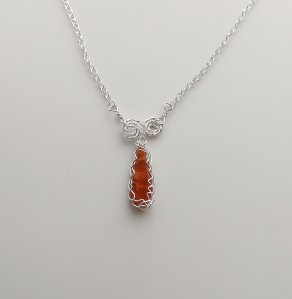 photo of an orange kyanite gemstone crystal from Tanzania, cut into a long teardrop shape and set into a pendant that has sterling silver Celtic style pattern wire plaid work around it