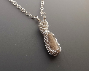 photo of a rhyolite rock from Utah, USA, which has topaz running through it, set into a pendant that has sterling silver celtic style pattern wire work around it