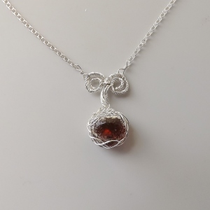 photo of a cognac brown amber from Sumatra Indonesia, chunky round cabochon cut and set into a pendant that has sterling silver Celtic style pattern wire plaid work around it