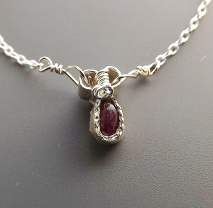 photo shows a tiny semi oval shape ruby which was mined in Norway. It is an almost opaque dark pink-red colour, and set into a hand textured bezel style sterling silver pendant