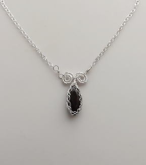 photo of ablack Whitby jet gemstone from England UK, cut into a marquise smooth shape and set into a pendant that has sterling silver Celtic style pattern wire plaid work around it