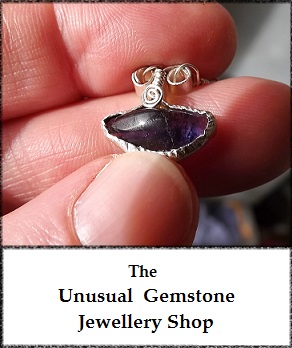 advert image shows a hand holding a rare blue john fluorite gemstone silver pendant, with the words "the unusual gemstone jewellery shop" underneath the main image